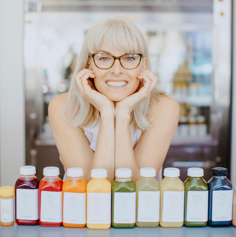 A woman sitting in front of many bottles of juice.