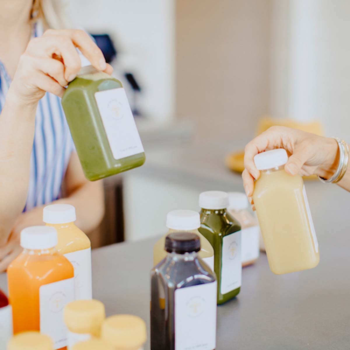 Two women are holding up bottles of juice.